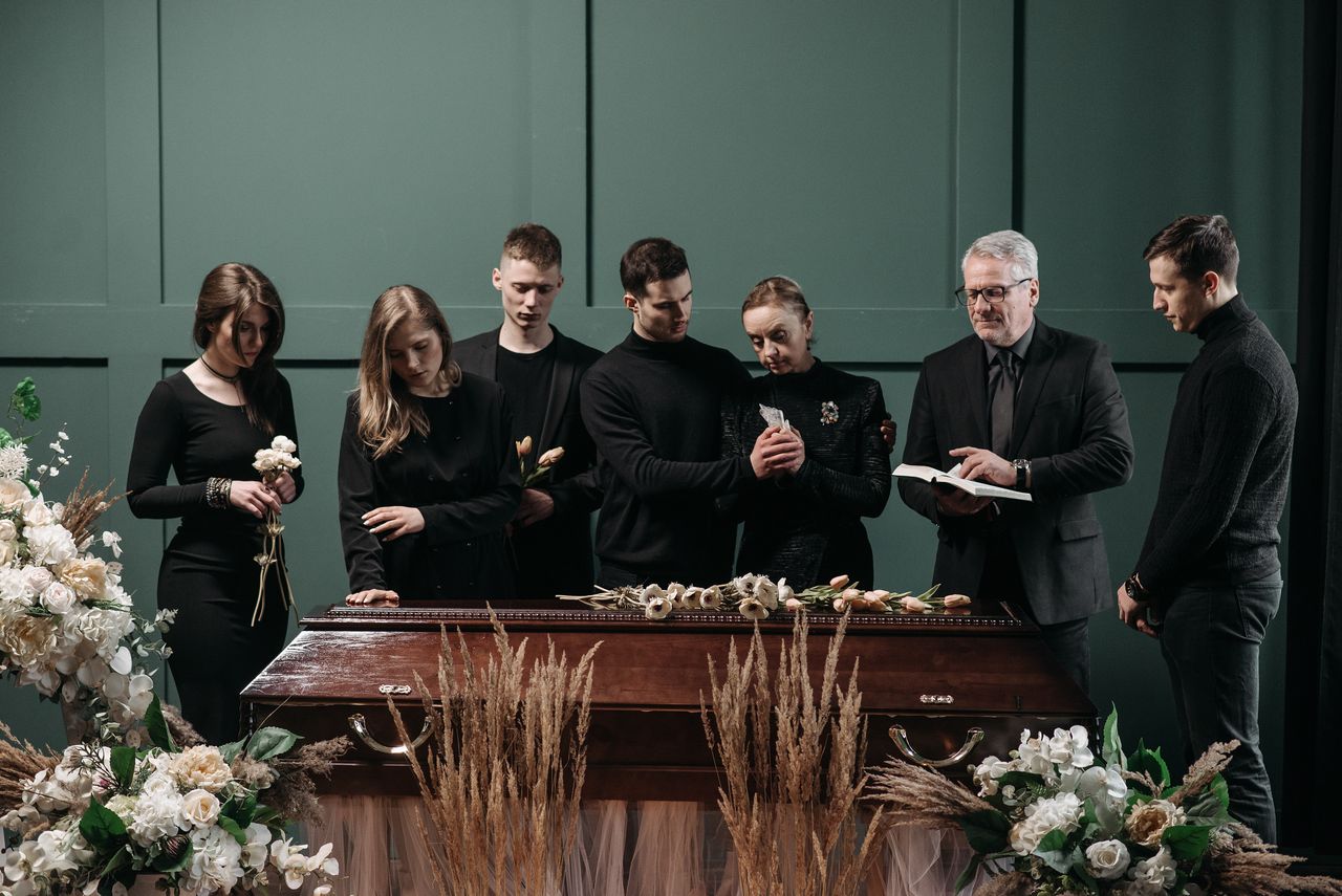 Inicio A funeral gathering with adults in a solemn indoor setting around a coffin, symbolizing loss and remembrance.